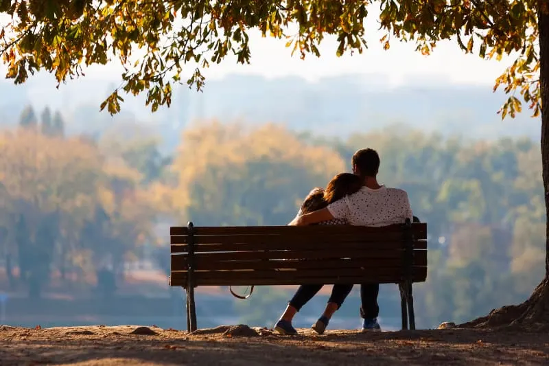 back view of man hugging her woman on park bench
