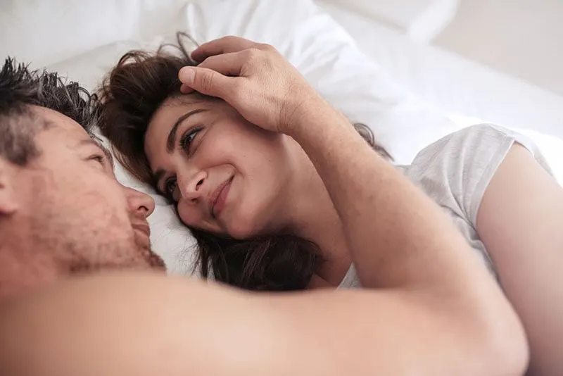 man cuddling with woman in bed