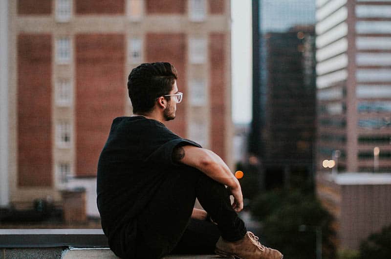 vista lateral de um homem de óculos e t-shirt preta sentado num telhado