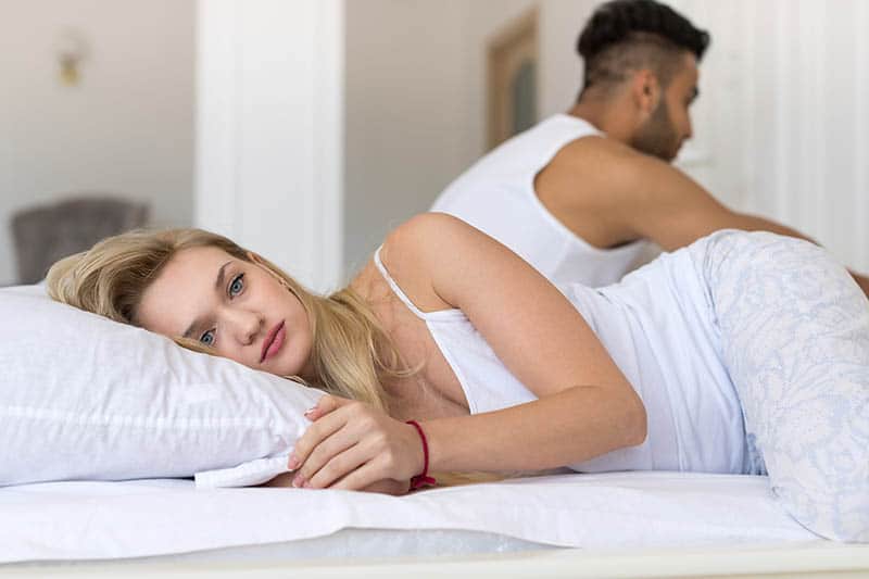 thoughtful woman lying on bed beside man