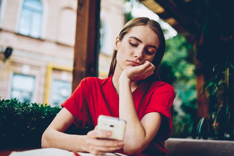 mujer pensativa con camiseta roja y mirando el móvil en una cafetería