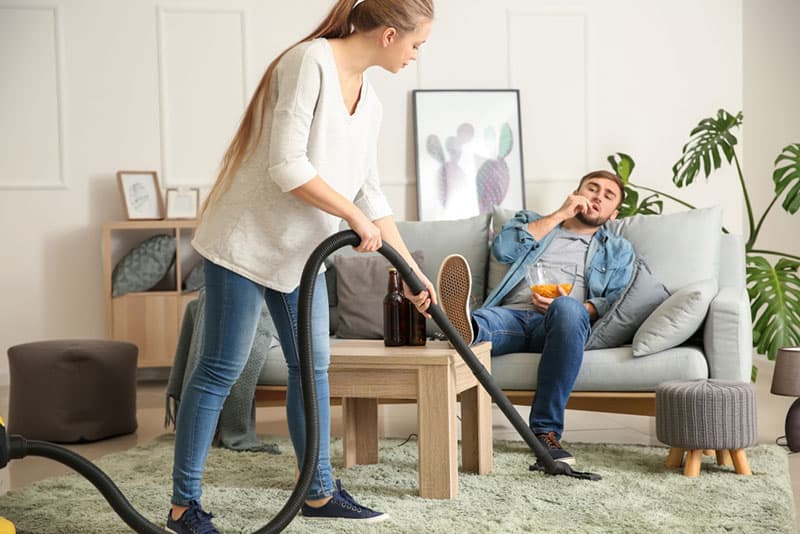 woman cleaning floor while her boyfriend watching tv