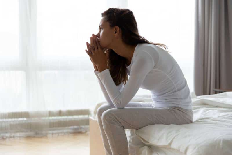 worried woman sitting on bed in bedroom