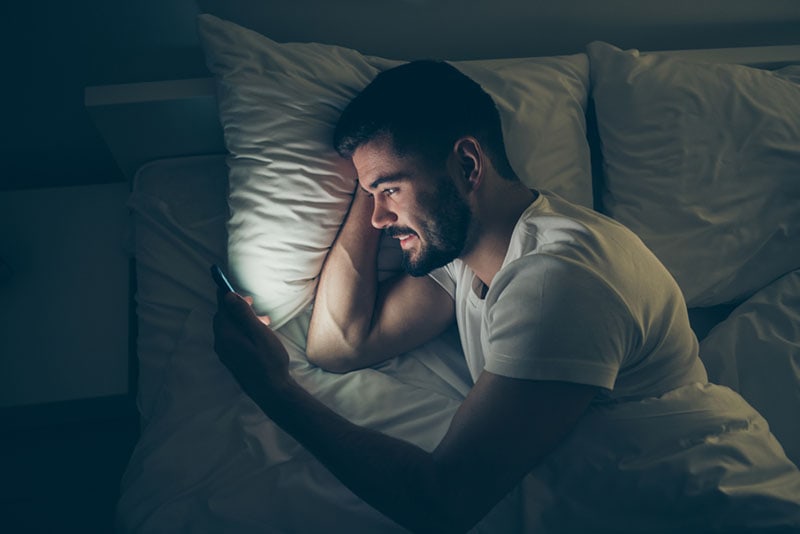 giovane uomo con il telefono in mano e sdraiato a letto