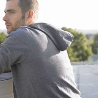 thoughtful young man leaning on wall looking away