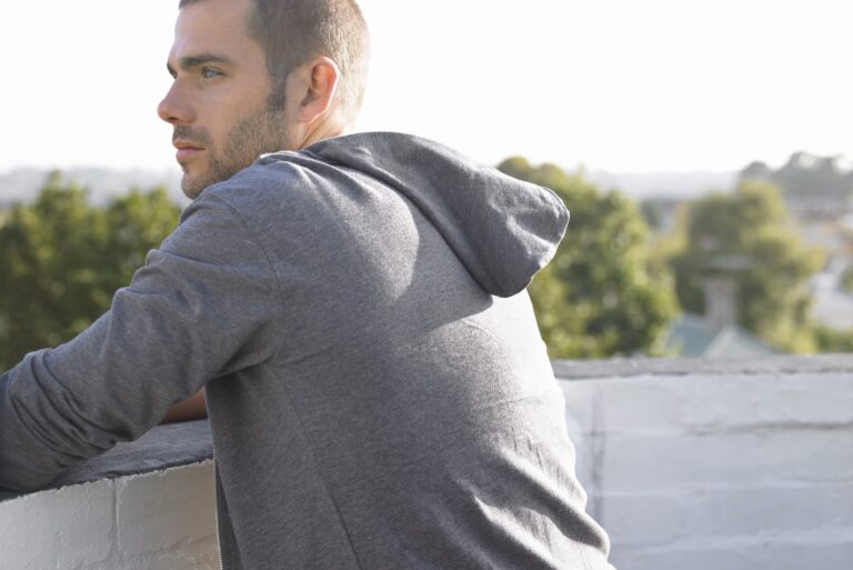 thoughtful young man leaning on wall looking away