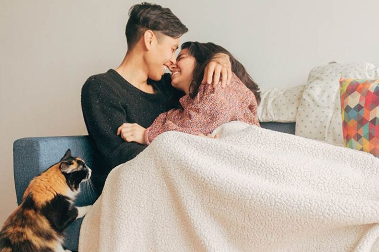 smiling couple cuddling under blanket at home