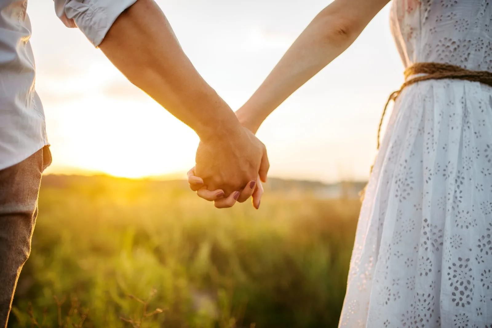 Couple hold hands in green field 