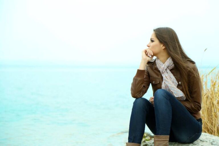 thoughtful woman sitting beside sea