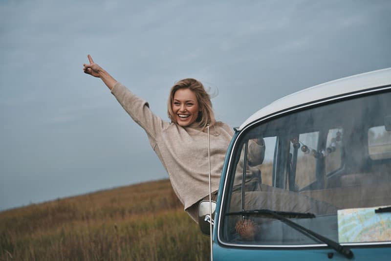 Young smiling woman leaning out the van's window and enjoying life