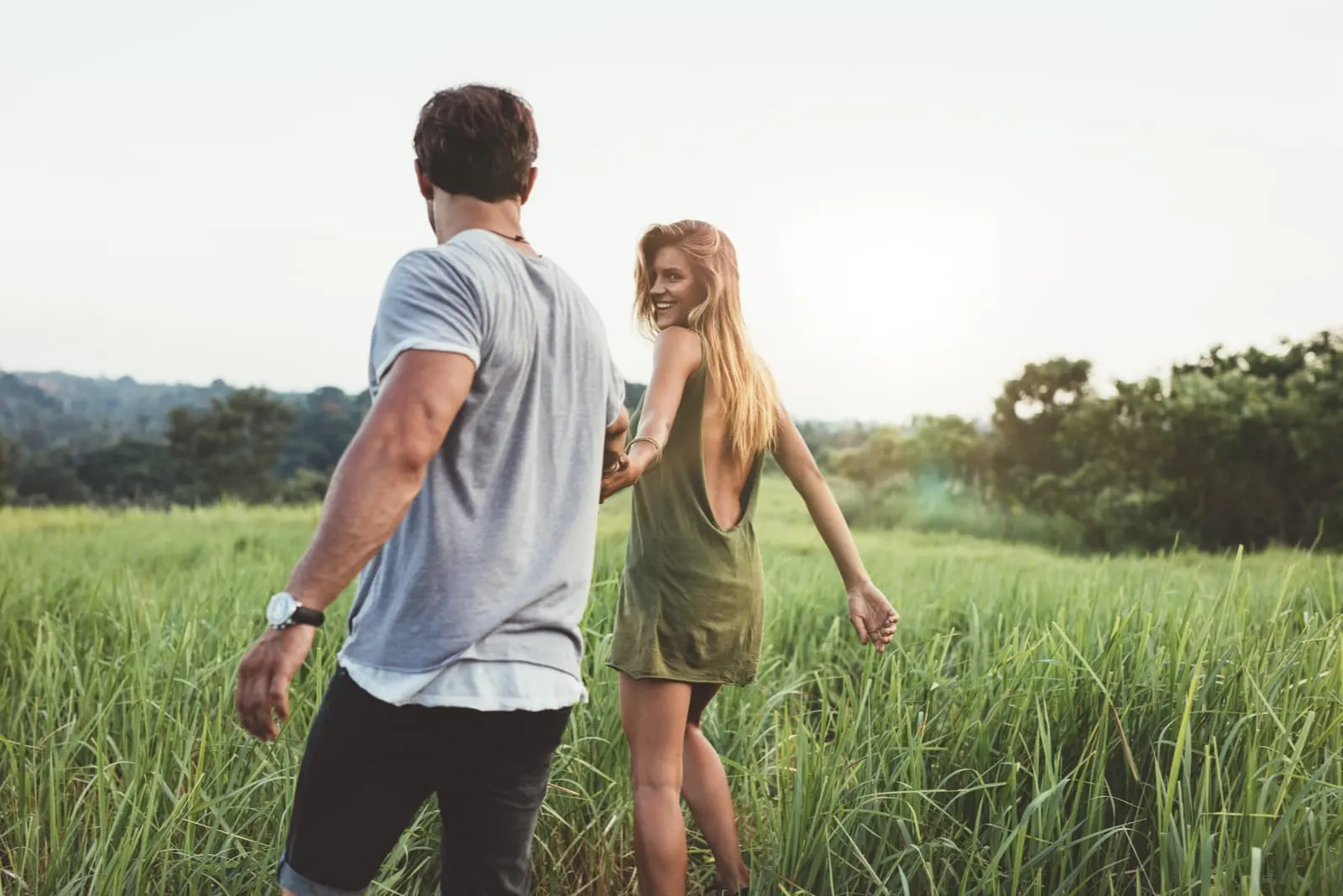 a man and a woman walk through the field holding hands