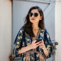 young, attractive and beautiful woman wearing a dress and sunglasses with her smartphone