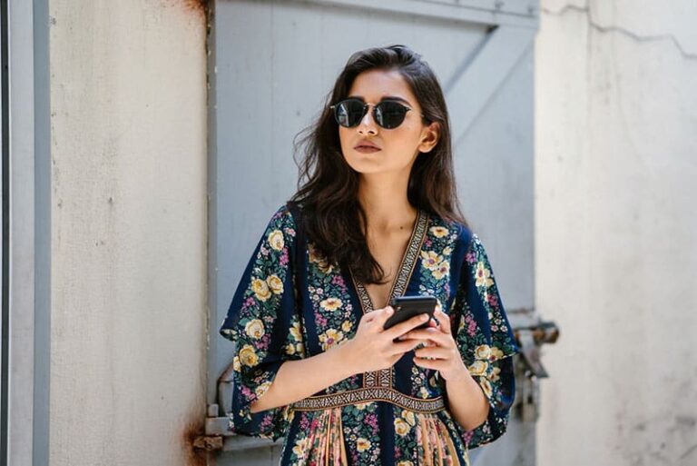 young, attractive and beautiful woman wearing a dress and sunglasses with her smartphone