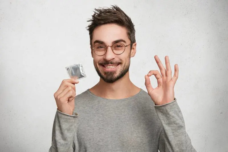 man holds condom and shows ok sign