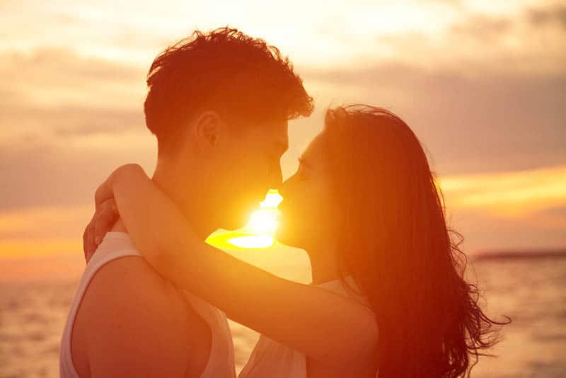 romantic couple hugging beside sea during golden hour