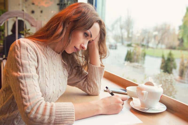 sad depressed woman writing a letter in cafe