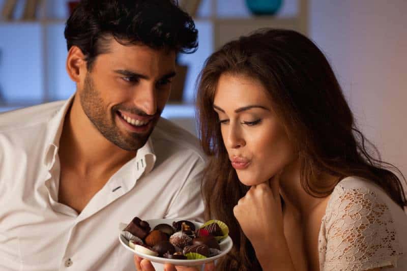 smiling man offering chocolate to woman