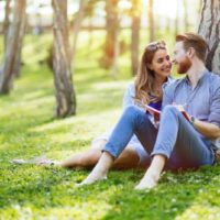 lovely couple sitting on grass and leaning on tree