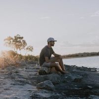 hombre sentado en una roca junto al agua
