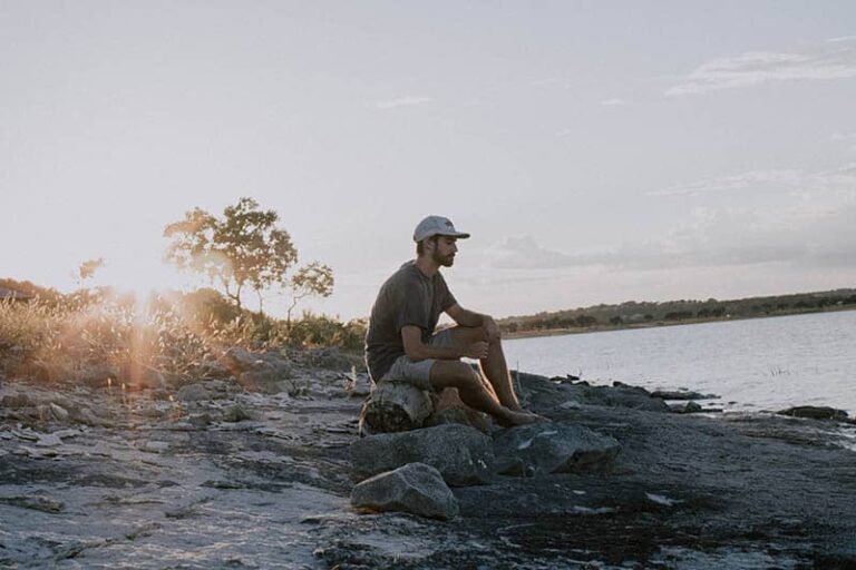 man sitting on rock beside water
