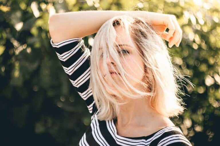 blonde woman standing outside with black and white shirt with hair covered her face