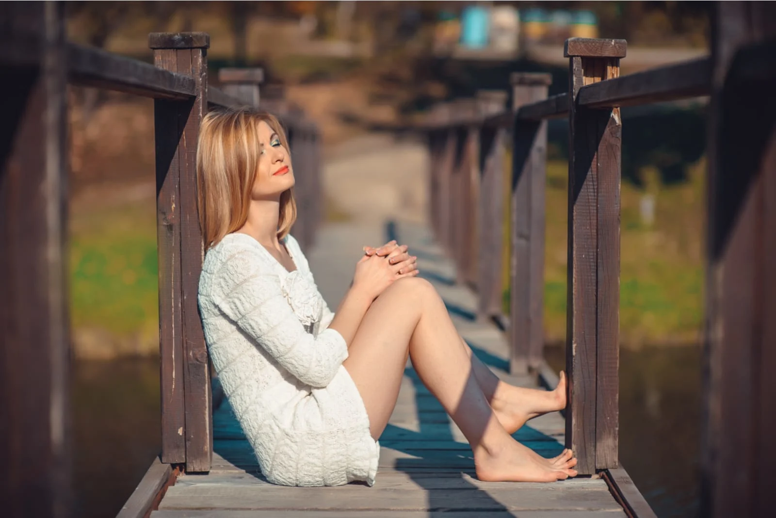 an attractive blonde sits on an old wooden bridge
