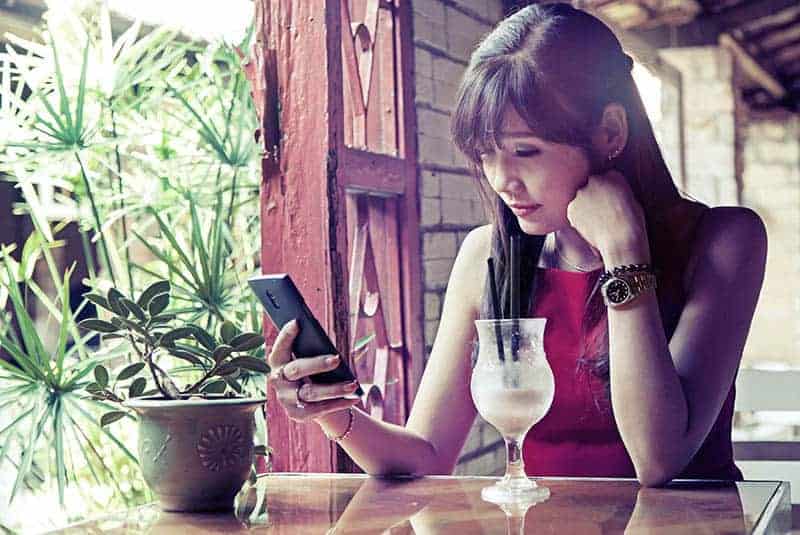 donna asiatica che scrive al telefono in un caffè