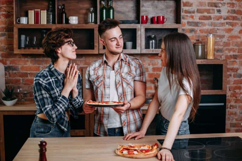 man between two women holding a pizza