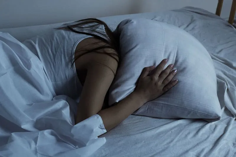 sad woman covering her head with pillow