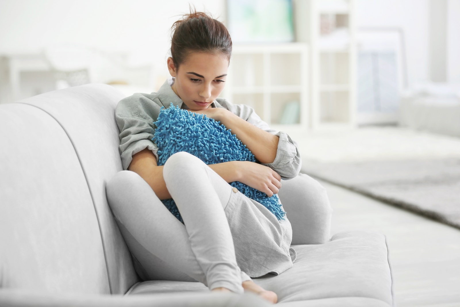sad woman sitting on the couch and hugging pillow