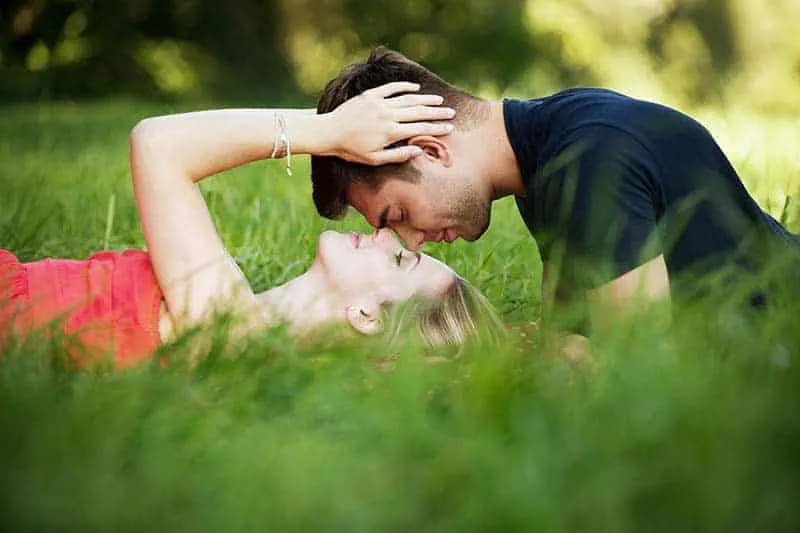 woman lying on grass field while man is over her face