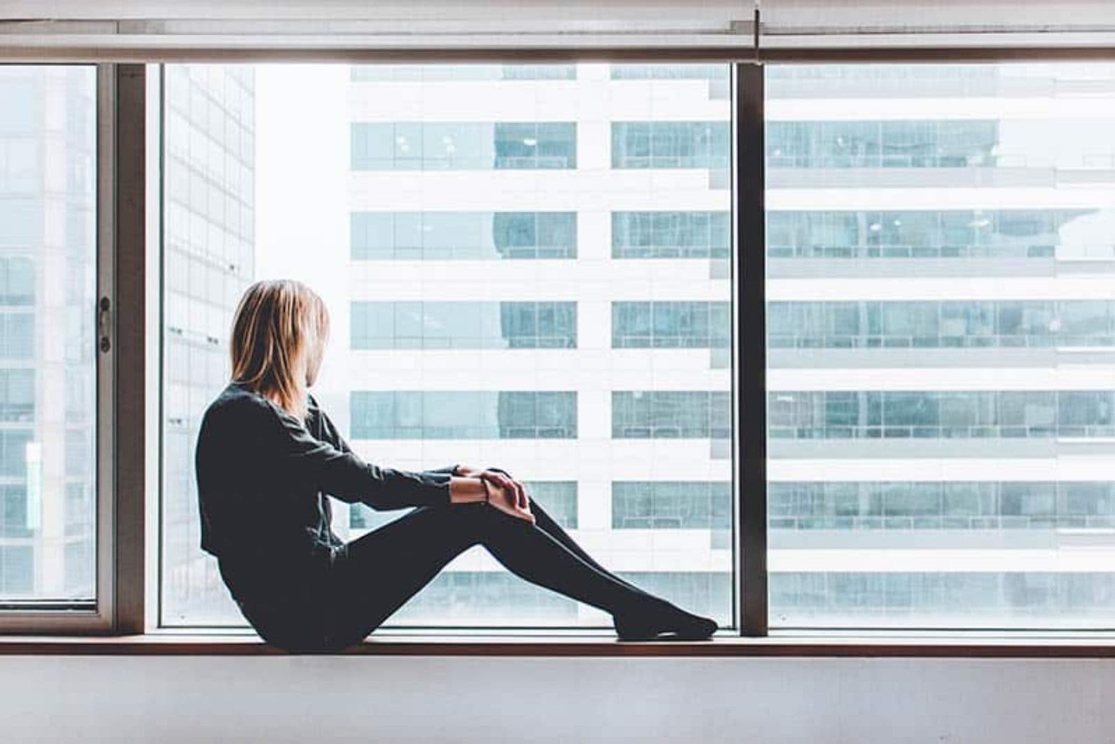 mujer preocupada sentada en el alféizar de la ventana