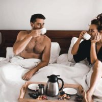lovely couple having a coffee on bed and talking
