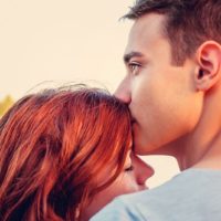 young man kissing woman forehead