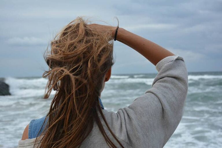 vista trasera de mujer se toca el pelo de pie frente al mar