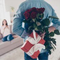 man surprising woman with flowers and gift