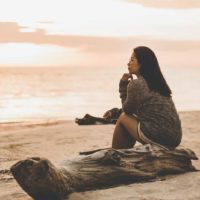 a lonely woman sitting on the beach at sunset