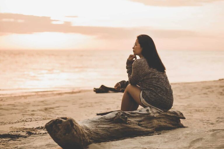 una donna sola seduta sulla spiaggia al tramonto