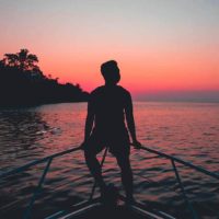 silhouette of man sitting on boat fence during night