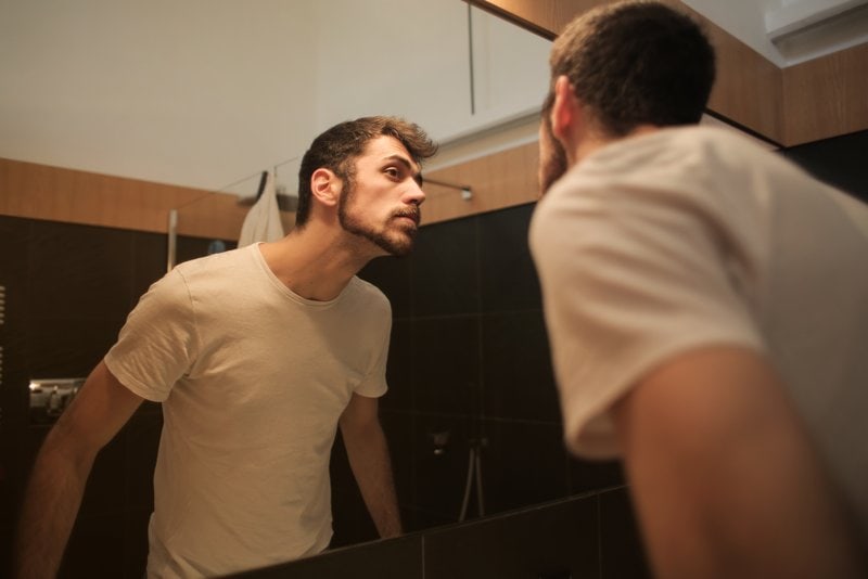 a man in a white T-shirt in the bathroom looks in the mirror