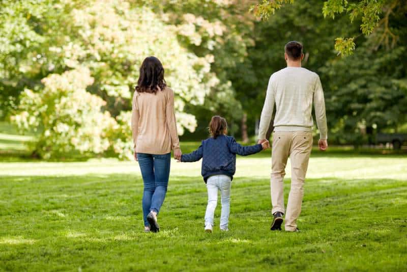 back view of parents holding daughter and walking on the grass field