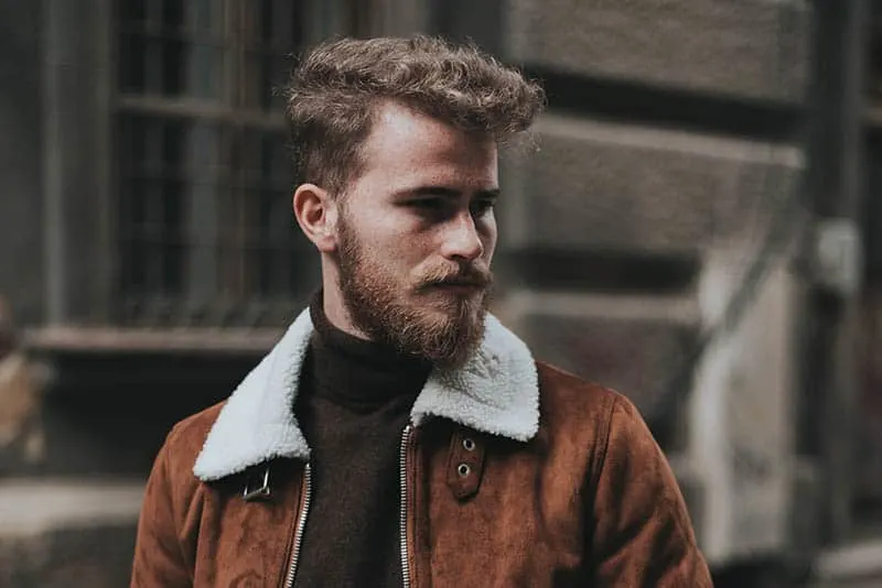 bearded man wearing brown jacket outside