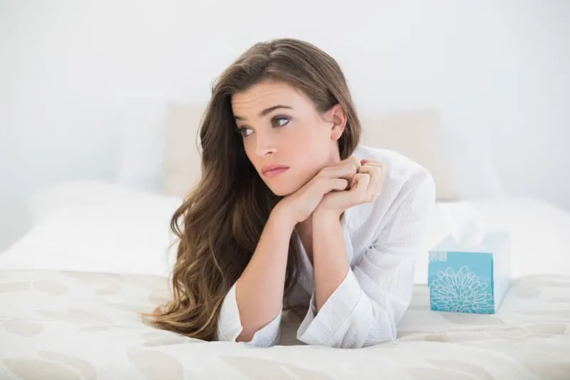 beautiful woman laying on bed with box of tissues