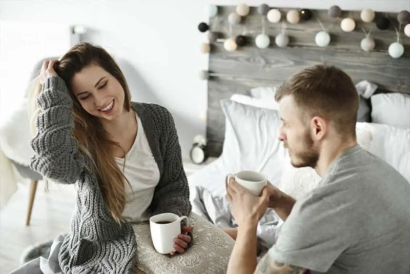 couple holding cup of tea and talking in bedroom