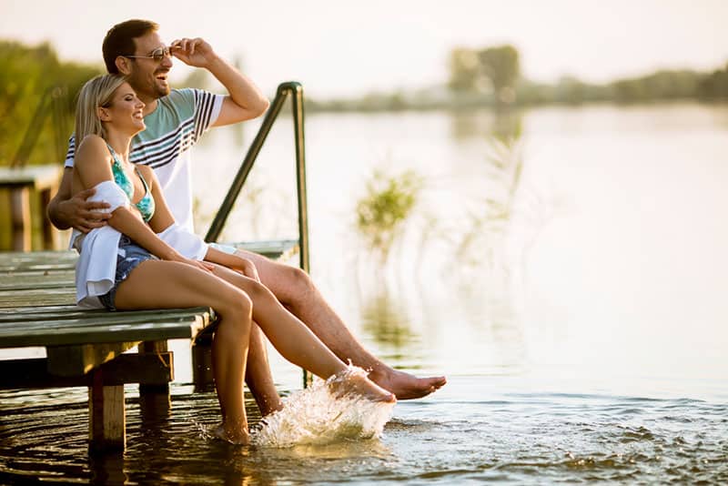 pareja sentada en el muelle junto al lago