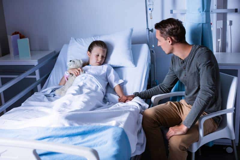 padre seduto accanto alla figlia distesa su un letto in ospedale
