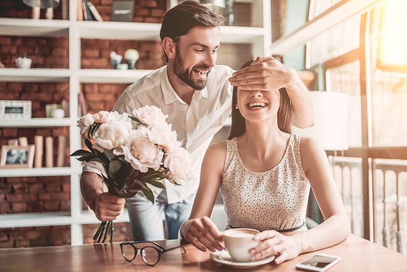 hombre feliz sorprendiendo a mujer con flores