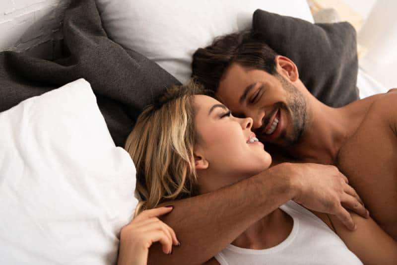 coppia sorridente che si abbraccia nel letto al mattino