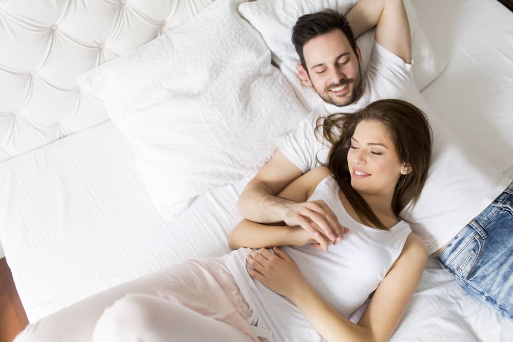 coppia sorridente sdraiata sul letto che parla