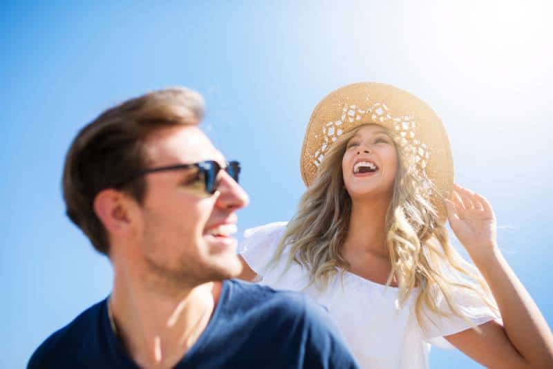 mujer sonriente con sombrero de pie detrás de un hombre feliz